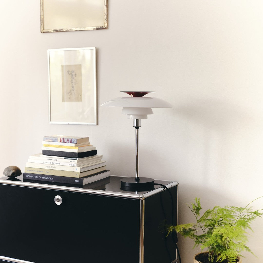 White lamp with red accent atop a black base, surrounded by stacked books on a sleek black surface.