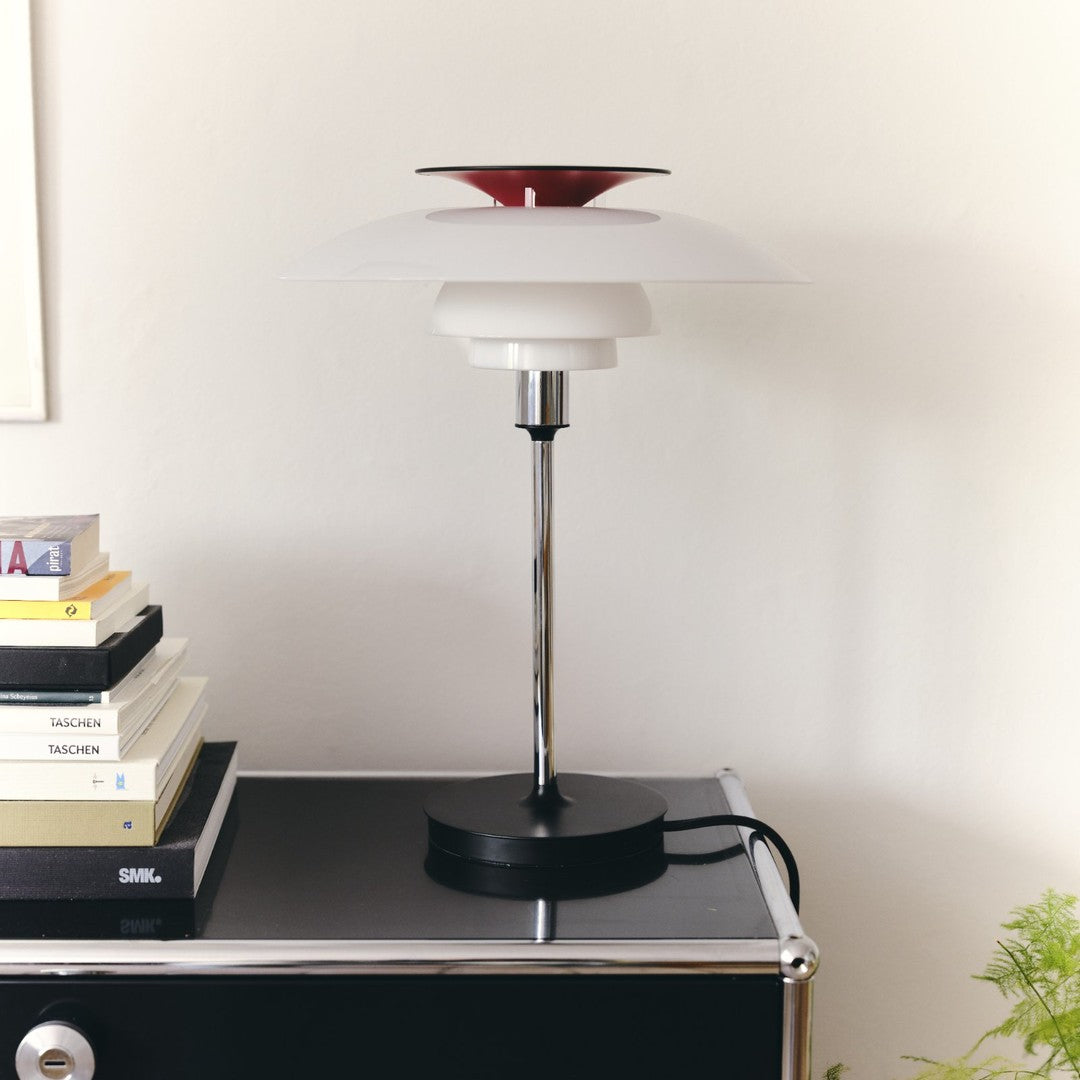 Red and white stacked lampshade with a sleek chrome stand atop a black table, surrounded by colorful book spines.