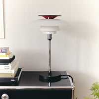 Red and white stacked lampshade with a sleek chrome stand atop a black table, surrounded by colorful book spines.