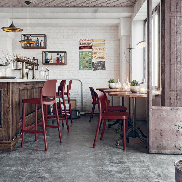 "Modern bar stools in deep red with a rustic wooden bar and gray concrete flooring, featuring stylish urban decor."