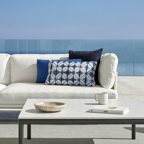 Navy blue, white, and aqua cushions with geometric patterns on a white outdoor sofa, enhancing a modern coastal vibe.