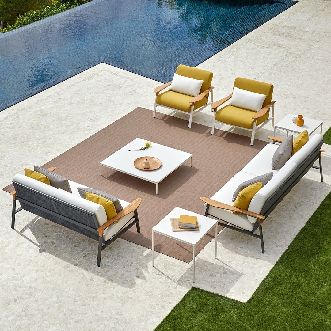 Modern outdoor seating set with gray and white sofas, yellow cushions, and geometric patterned rug by a pool.