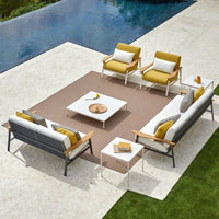 Modern outdoor seating set with gray and white sofas, yellow cushions, and geometric patterned rug by a pool.