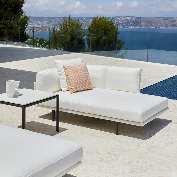 White outdoor lounge furniture with coral patterned cushion on a sleek surface by a pool, overlooking a scenic view.