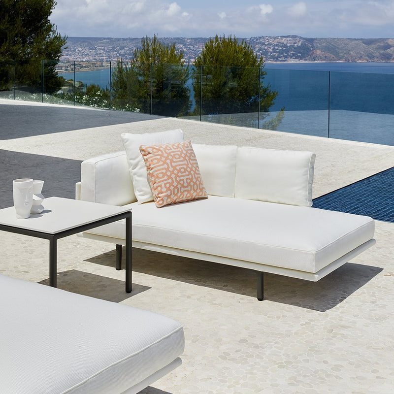 White outdoor lounge furniture with coral patterned cushion on a sleek surface by a pool, overlooking a scenic view.