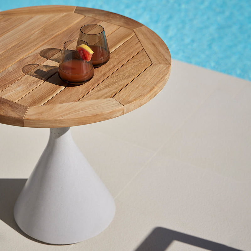 Round wooden table with a natural finish and a white cone base, set against a vibrant blue pool background.