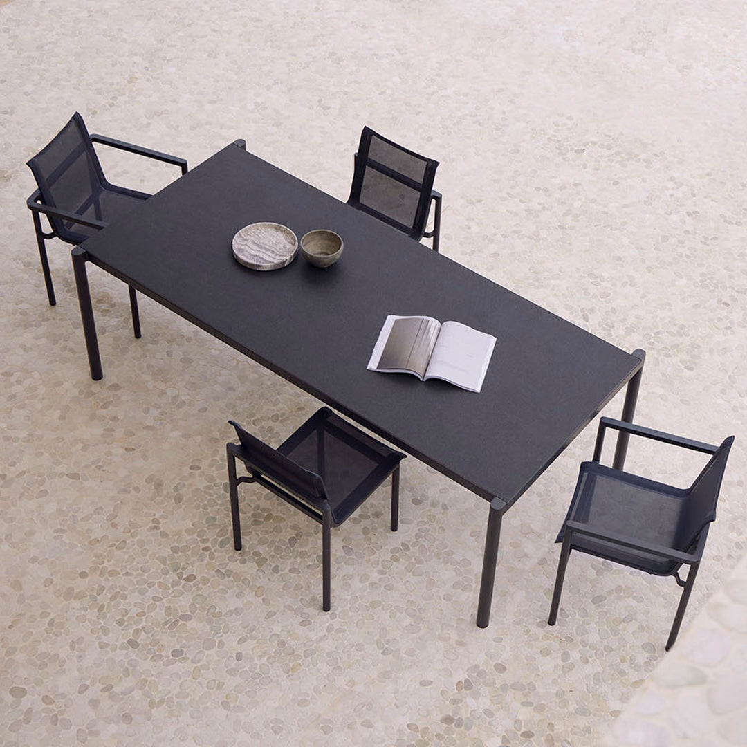 Modern black rectangular table with matching mesh chairs, set on a light, textured floor.