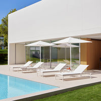 White lounge chairs with matching umbrellas by a pool, featuring a minimalist design against a modern building backdrop.