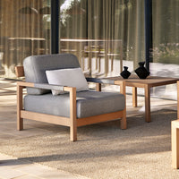 Gray upholstered chair with a minimalist wooden frame, paired with a light-colored table and earthy woven rug.