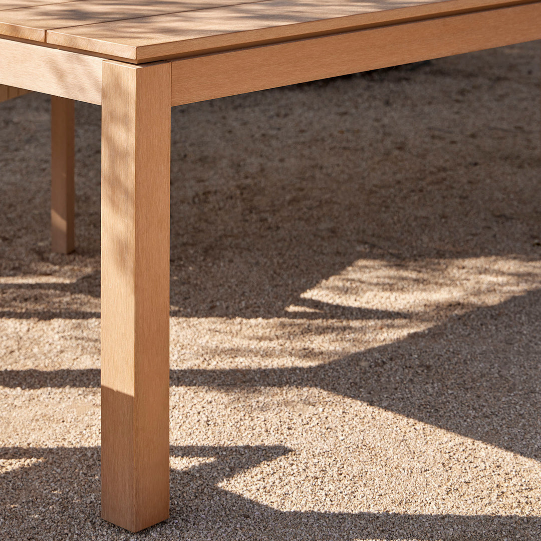 Light wood table with a smooth finish, casting soft shadows on a textured sandy surface.