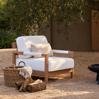 "Modern white outdoor chair with light wooden frame, paired with neutral decor elements in a sandy environment."