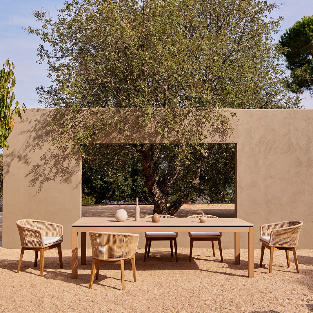 Stylish outdoor dining set featuring a natural wood finish and woven beige chairs against a serene earthy backdrop.