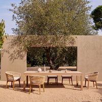 Stylish outdoor dining set featuring a natural wood finish and woven beige chairs against a serene earthy backdrop.