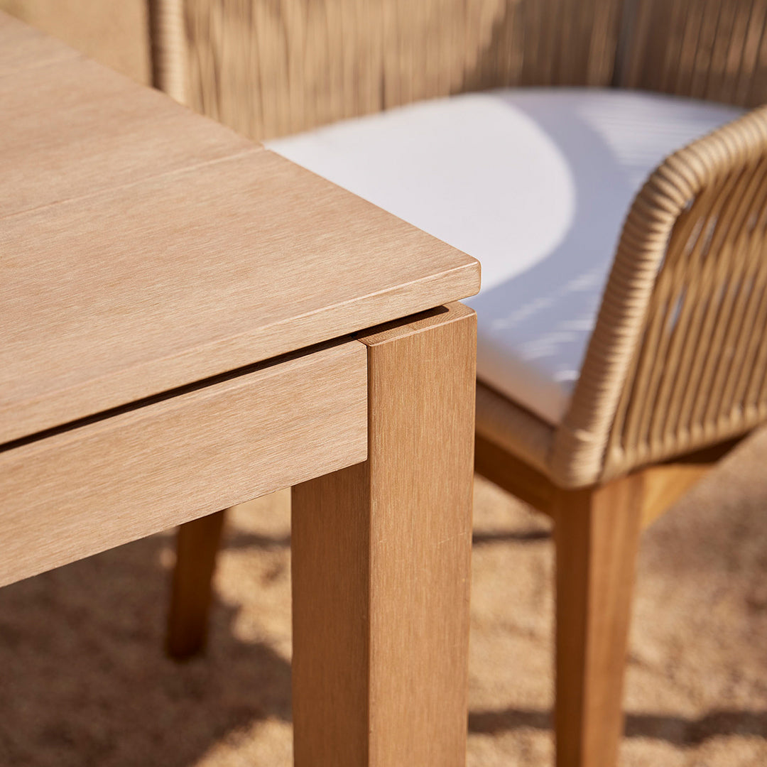 Light oak wooden table with a sleek finish, paired with a beige woven chair and white cushion for a modern look.