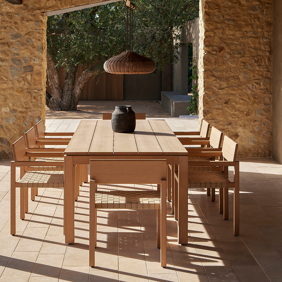 Natural wood dining table with woven chairs, featuring warm tones and a textured, rustic stone backdrop.