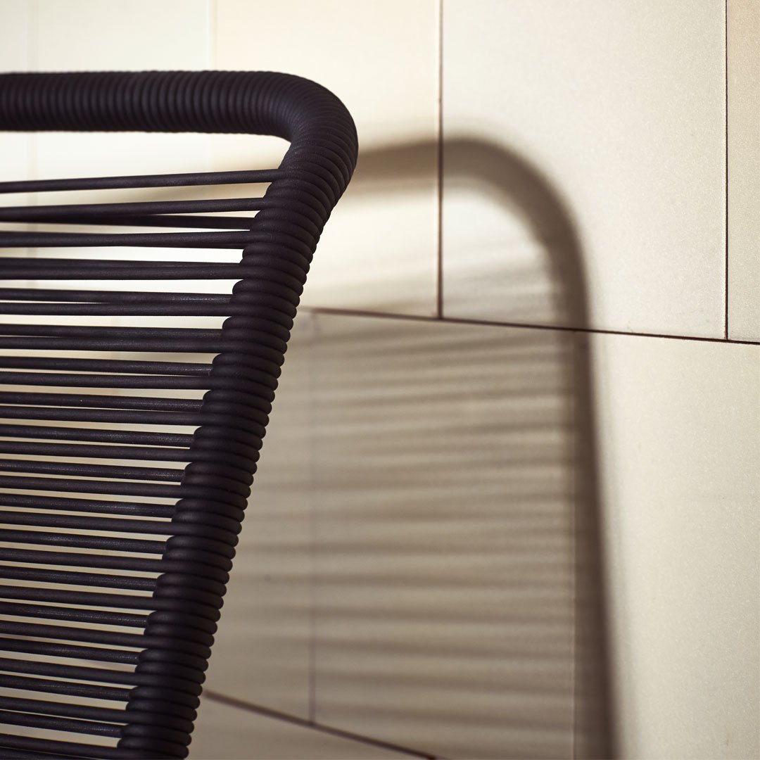 Black striped chair with shadow against a light-colored wall, showcasing a modern minimalist design.
