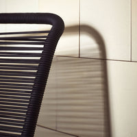 Black striped chair with shadow against a light-colored wall, showcasing a modern minimalist design.