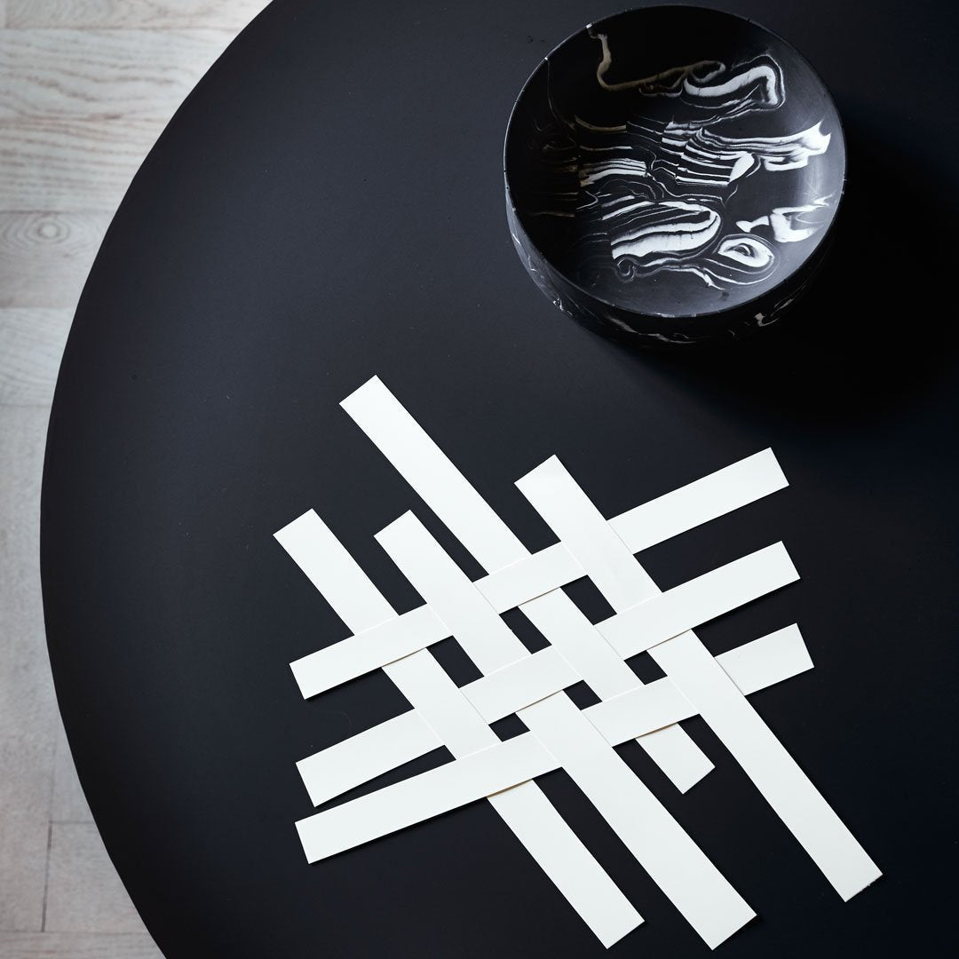White geometric lines arranged in a woven pattern on a black table. Modern design with sleek contrast.