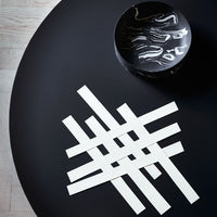 White geometric lines arranged in a woven pattern on a black table. Modern design with sleek contrast.
