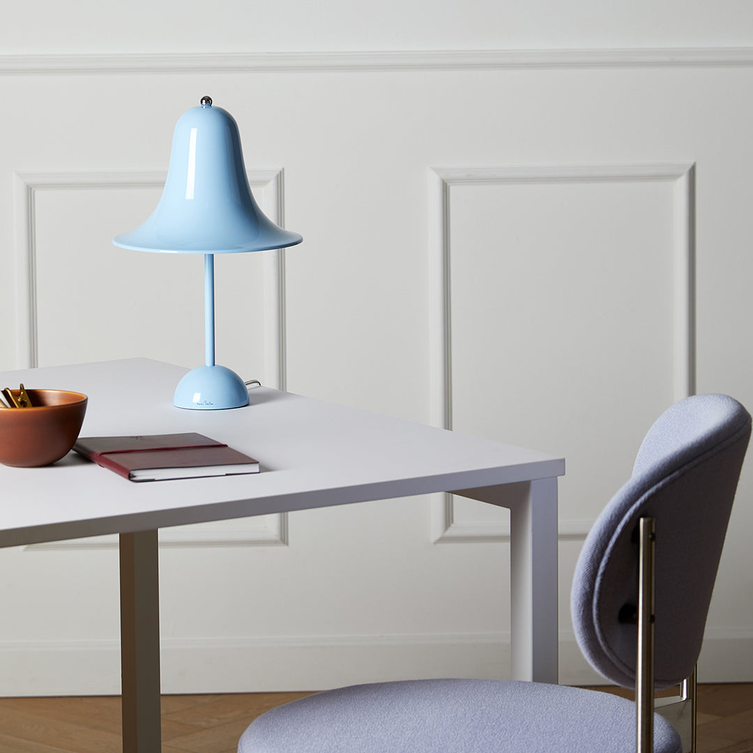 Light blue lamp on a minimalist white desk, with a lavender chair and earthy brown bowl, creating a serene workspace.