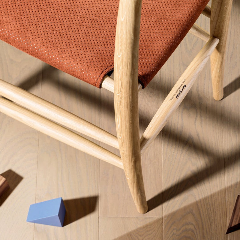 Rust-colored perforated seat fabric with natural wood frame on light wooden floor, featuring colorful geometric blocks.