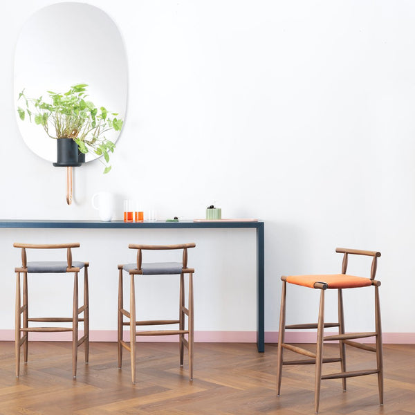 Modern wooden bar stools with orange and grey cushions, set against a minimalist white wall and wooden floor.