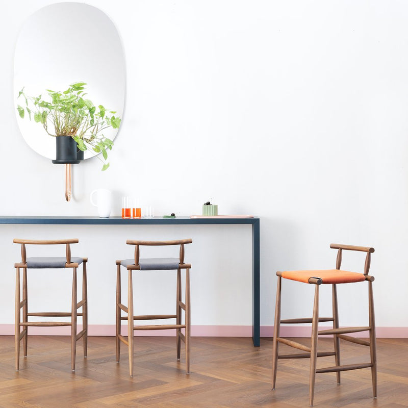 Modern wooden bar stools with orange and grey cushions, set against a minimalist white wall and wooden floor.