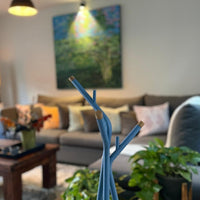 Blue decorative branches with gold tips against a cozy, light-filled living room backdrop featuring soft pastel accents.