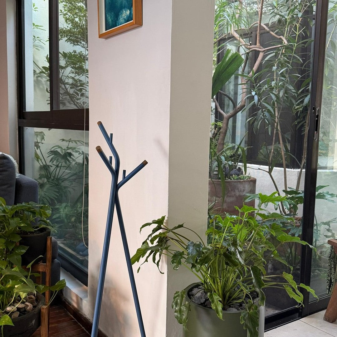 "Stylish blue coat rack with a minimalist design against a backdrop of green plants and natural light."