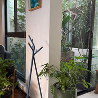 "Stylish blue coat rack with a minimalist design against a backdrop of green plants and natural light."