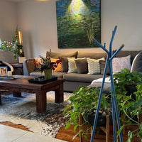 "Cozy living room with blue accents, textured cushions, green plants, and a colorful abstract painting."