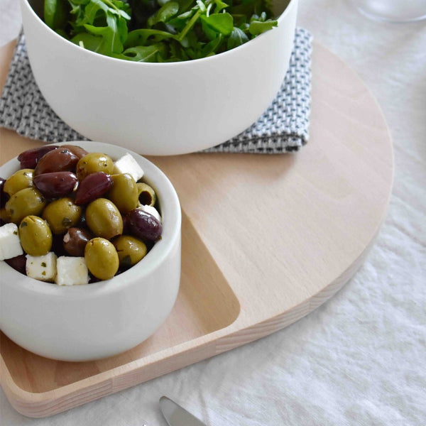 White circular bowls with olives and feta on a light wood tray; green salad in a white bowl on a patterned napkin.