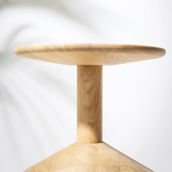 Light oak wood stool with a smooth round top and geometric base, showcasing natural grain patterns.