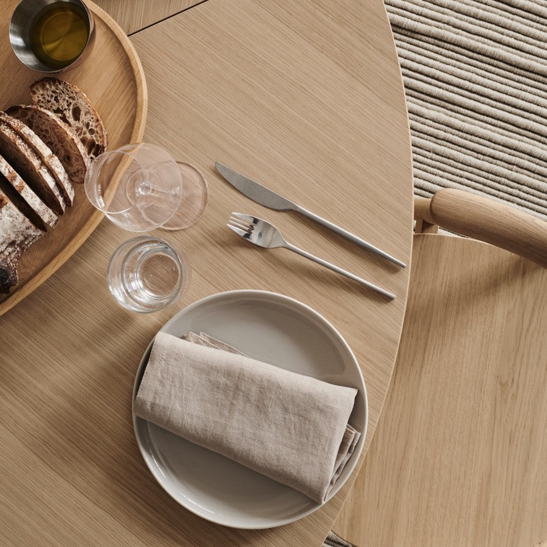Elegant wooden table setting with neutral-toned plate, linen napkin, clear glassware, and rustic woven basket.