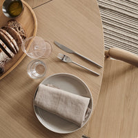Minimalist table setting featuring earthy tones, soft grey napkin, sleek silver cutlery, and a textured wooden surface.