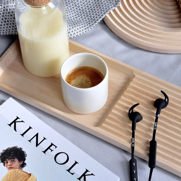 "Neutral tones with a textured wooden tray, white cup, and black earphones amidst soft fabrics."