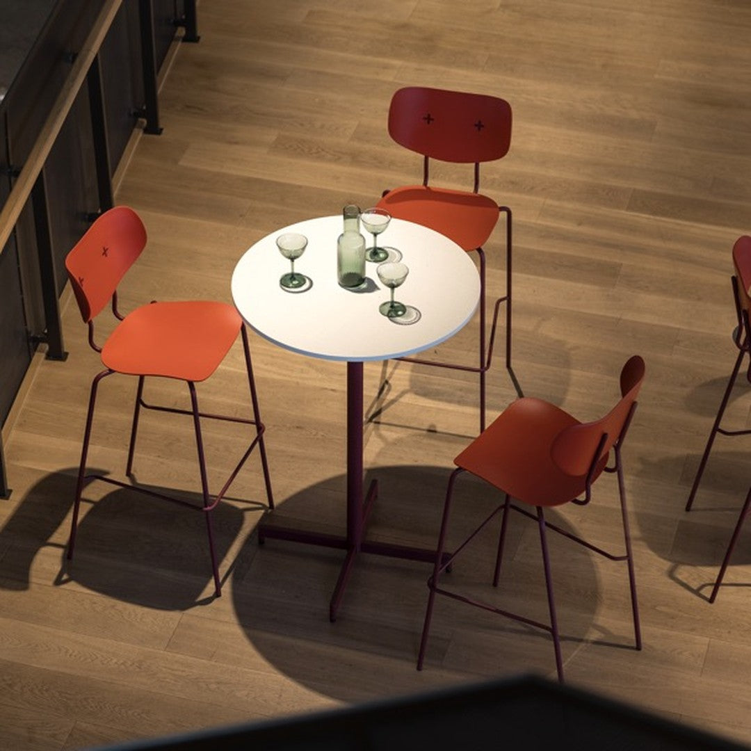 Red chair and white round table set against a warm wood floor, featuring green glassware for a modern aesthetic.