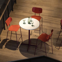 Red chair and white round table set against a warm wood floor, featuring green glassware for a modern aesthetic.