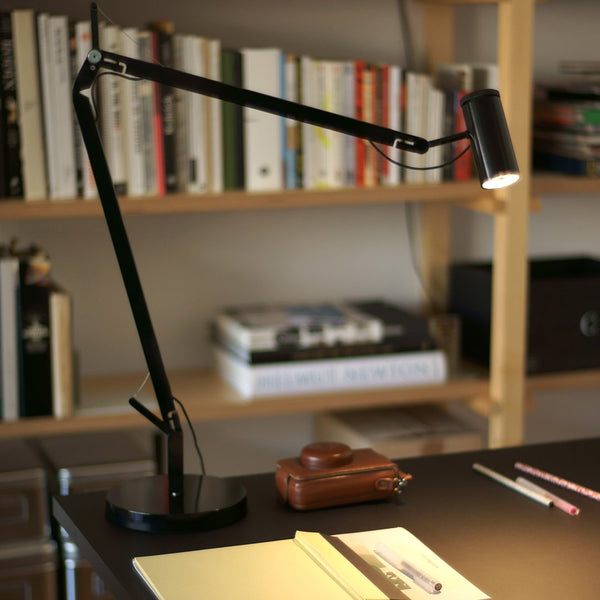 Black adjustable desk lamp with a sleek, modern design on a dark wooden table surrounded by books.