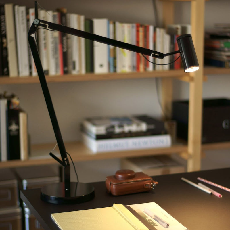 Black adjustable desk lamp with a sleek, modern design on a dark wooden table surrounded by books.