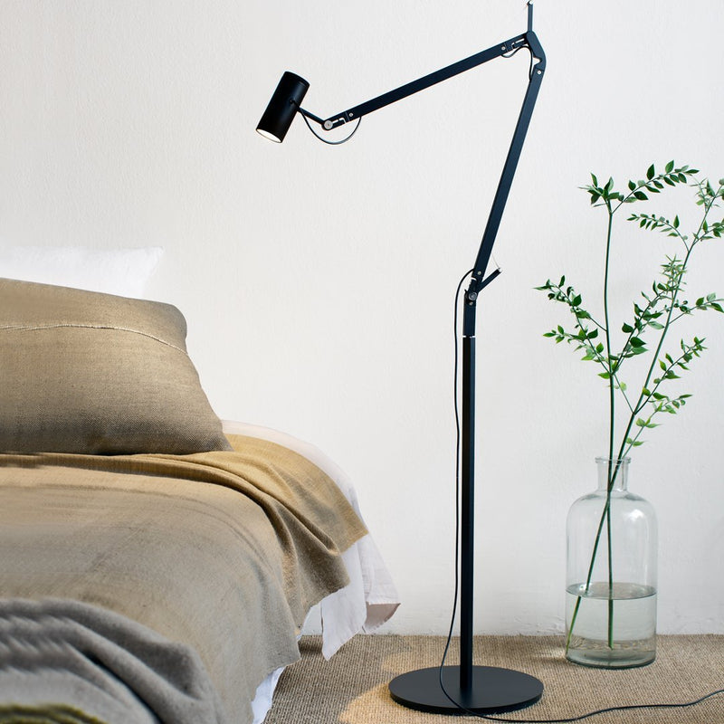 Modern black floor lamp with sleek design, complemented by a neutral beige throw and soft textures.