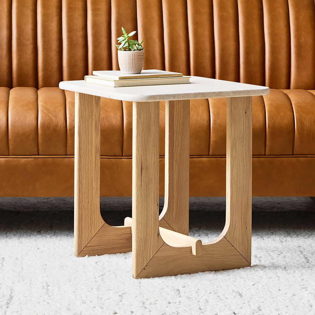 Light wood side table with a white marble top, set against a rich brown leather sofa and a neutral rug.