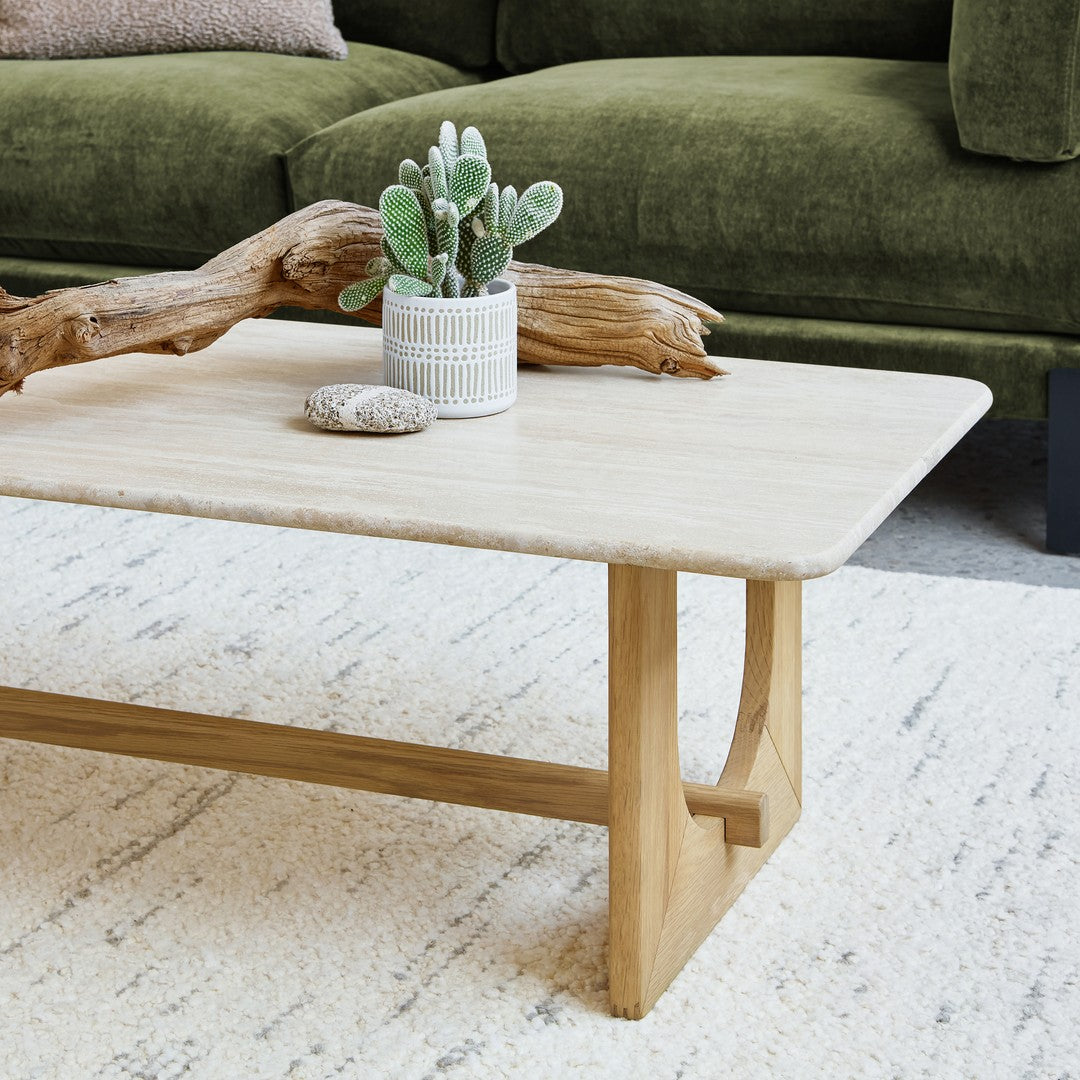 Light beige coffee table with natural wood legs, complemented by green succulent and olive couch. Soft, textured rug.