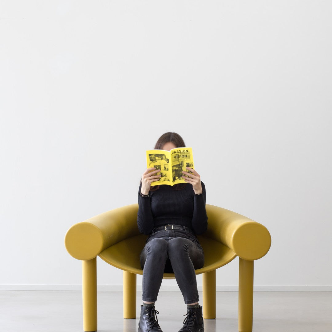 Yellow modern chair with smooth, curved lines against a minimalist white background. Individual reading a yellow book.