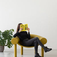 Yellow contemporary chair with a smooth finish, paired with black clothing and a vibrant yellow magazine.