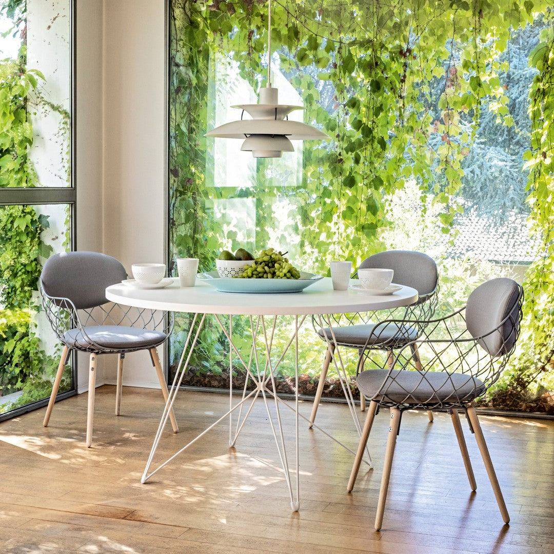 Modern round table with white top, gray chairs, and vibrant green foliage in a bright indoor setting.