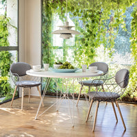 Modern round table with white top, gray chairs, and vibrant green foliage in a bright indoor setting.