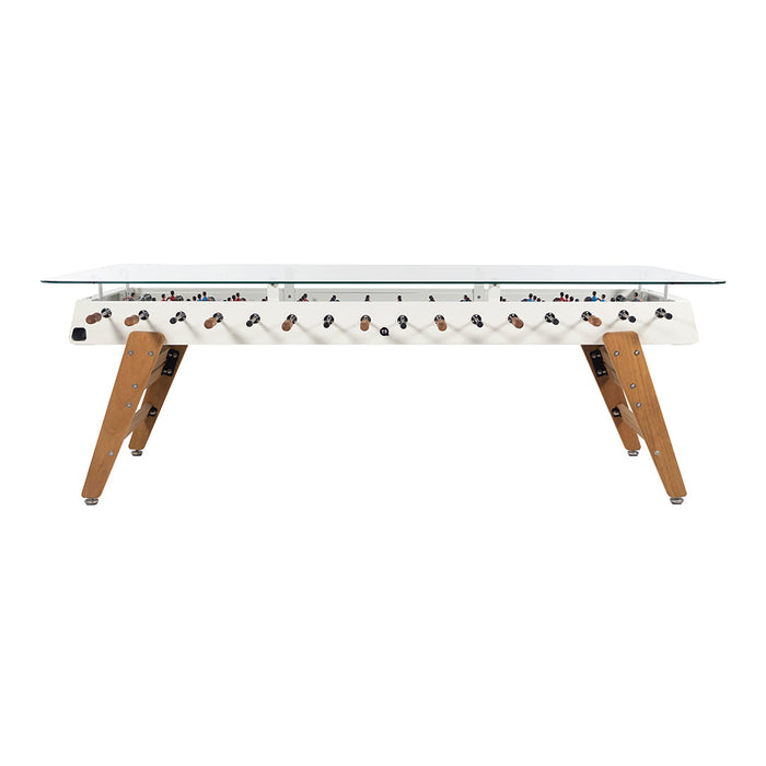 Modern glass-top foosball table with white body and natural wood legs, featuring colorful player figures.
