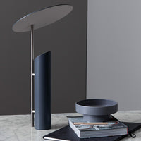 Sleek blue and gray modern lamp with minimalist bowl and stylish notebooks on a marble surface.