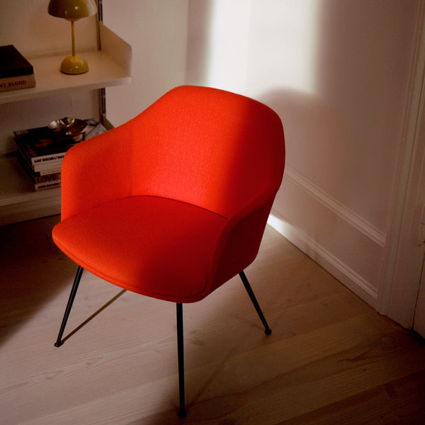 Vibrant red upholstered chair with sleek black legs, set against warm, natural light background. Perfect for modern decor.